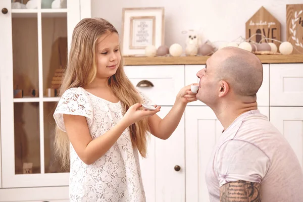 Adorável filha vestindo um vestido branco whith seu pai amoroso. Eles estão bebendo chá de um prato de brinquedo em uma moderna sala de crianças. Família feliz . — Fotografia de Stock