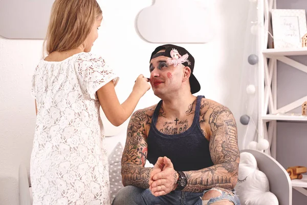 Grappige tijd tattoed vader in een GLB en zijn kind spelen thuis. Schattig meisje doet make-up aan haar vader in haar slaapkamer. Familie vakantie saamhorigheid — Stockfoto