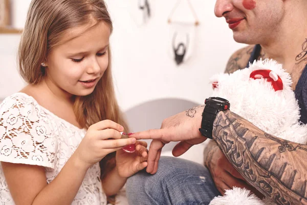 Legrační čas, tetování otec v čepici a jeho dítě si hrají doma. Roztomilá holka dělá make-up tátovi do ložnice. Rodinné svátky — Stock fotografie