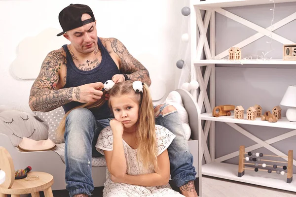 Temps drôle Tatoué père dans une casquette et son enfant jouent à la maison. Papa coiffe ses filles dans sa chambre. Vacances en famille et convivialité — Photo