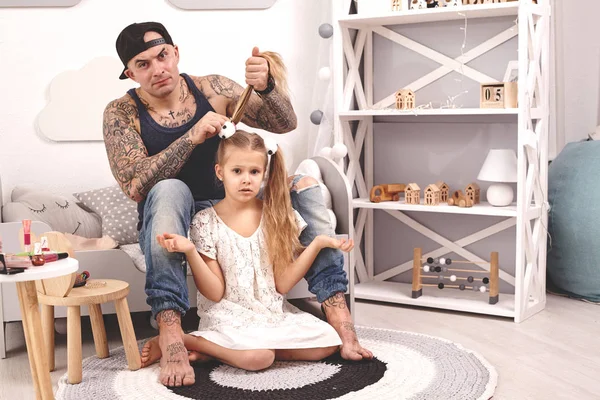 Legrační čas, tetování otec v čepici a jeho dítě si hrají doma. Táta dělá v ložnici své dcery vlasy. Rodinné svátky — Stock fotografie