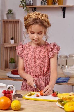 Modern bir saç modeli ile Sevimli güzel kız üzerinde raflar ile beyaz bir duvara karşı bir mutfakta yemek yapıyor.