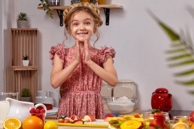 Modern bir saç modeli ile Sevimli güzel kız üzerinde raflar ile beyaz bir duvara karşı bir mutfakta yemek yapıyor.