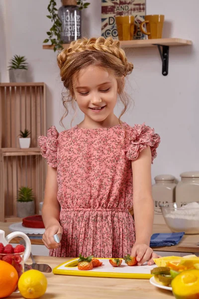 Menina bonita bonito com um penteado moderno está cozinhando em uma cozinha contra uma parede branca com prateleiras . — Fotografia de Stock