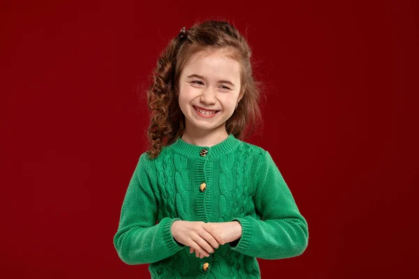 Retrato de una niña morena con el pelo largo y rizado posando sobre un fondo rojo . — Foto de Stock