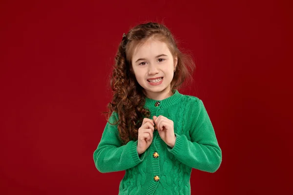 Retrato de una niña morena con el pelo largo y rizado posando sobre un fondo rojo . — Foto de Stock