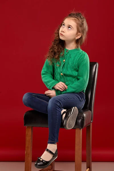 Retrato de una niña morena con el pelo largo y rizado posando sobre un fondo rojo . —  Fotos de Stock