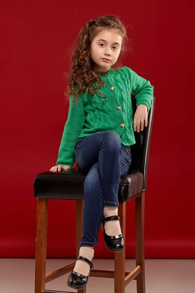 Portré egy kis barna lány, hosszú, göndör haja pózol ellen piros háttér. — Stock Fotó