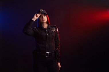 Ciddi kadın polis memuru kırmızı ve mavi arka aydınlatma ile siyah bir arka plan karşı kamera için poz.