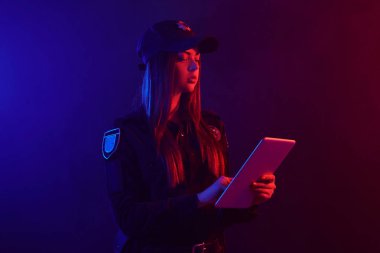 Kırmızı ve mavi arka aydınlatmalı siyah arka plan aleyhine kameraya poz veren bir kadın polis memurunun yakın çekim portresi.