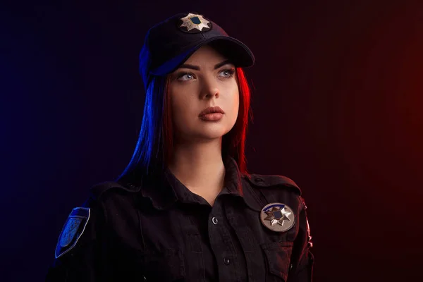 赤と青のバックライトを持つ黒い背景に対してカメラのためにポーズを取る深刻な女性警官のクローズアップショット. — ストック写真