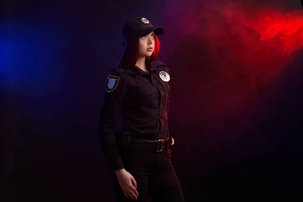 Serious female police officer is posing for the camera against a black background with red and blue backlighting. — Stock Photo, Image