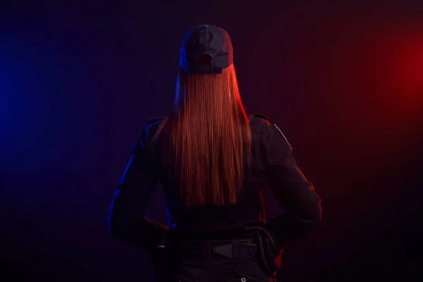 Súlyos női rendőr pózol a kamera ellen, fekete háttér, piros és kék háttérvilágítással. — Stock Fotó