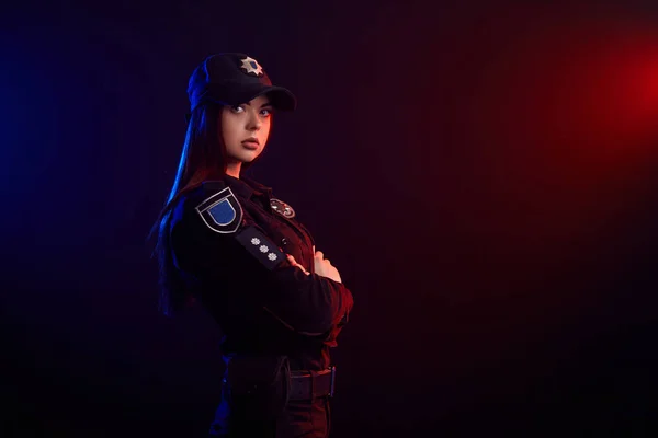 Allvarlig kvinnlig polis är poserar för kameran mot en svart bakgrund med röd och blå bakgrundsbelysning. — Stockfoto