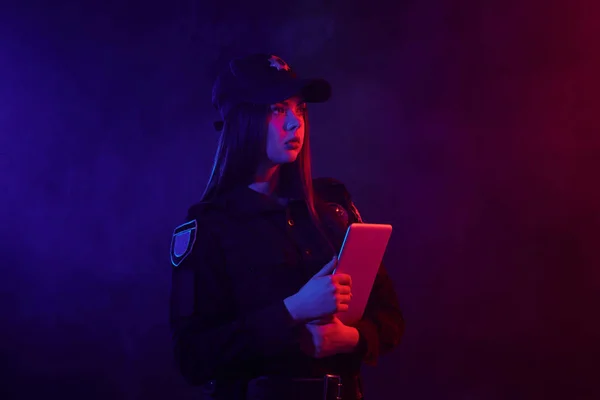 Ruiva policial do sexo feminino está posando para a câmera contra um fundo preto com backlighting vermelho e azul . — Fotografia de Stock