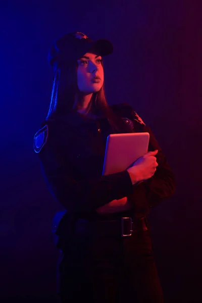 Vörös hajú női rendőr pózol a kamera ellen, fekete háttér, piros és kék háttérvilágítással. — Stock Fotó