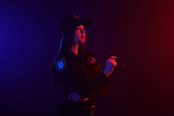 Une policière rousse pose pour la caméra sur un fond noir avec un rétroéclairage rouge et bleu . — Photo