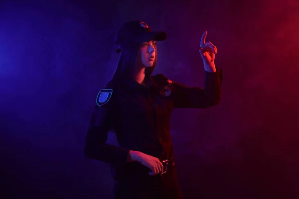 Punatukkainen naispoliisi poseeraa kameralle mustaa taustaa vasten punaisella ja sinisellä taustavalolla . — kuvapankkivalokuva
