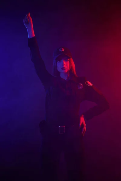 Ruiva policial do sexo feminino está posando para a câmera contra um fundo preto com backlighting vermelho e azul . — Fotografia de Stock