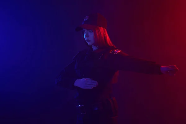 Une policière rousse pose pour la caméra sur un fond noir avec un rétroéclairage rouge et bleu . — Photo