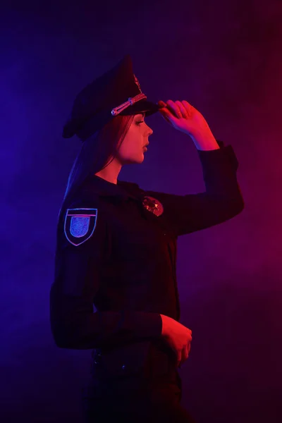 Mujer policía pelirroja posando para la cámara sobre un fondo negro con retroiluminación roja y azul . —  Fotos de Stock