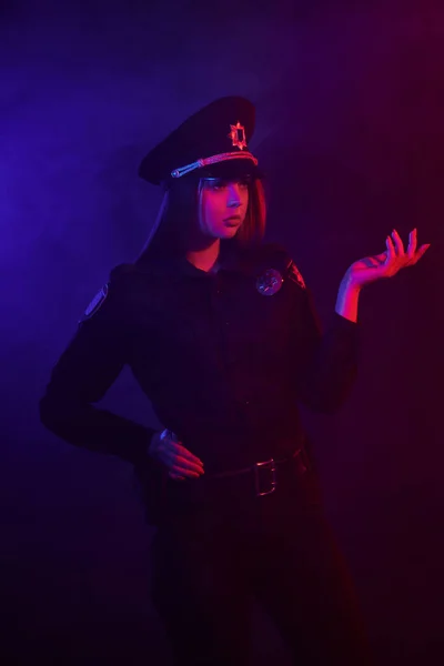 Vörös hajú női rendőr pózol a kamera ellen, fekete háttér, piros és kék háttérvilágítással. — Stock Fotó