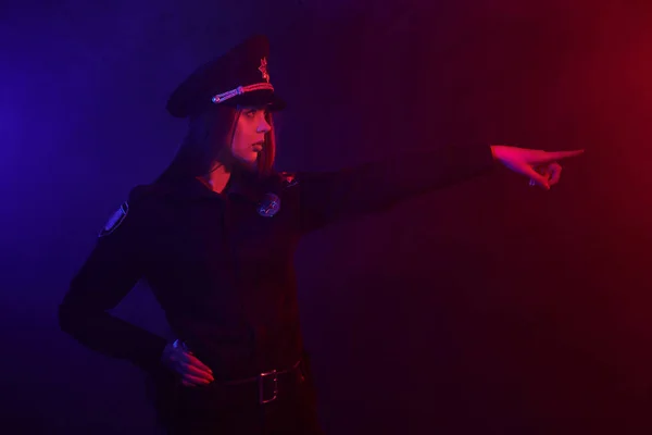 赤毛の女性警察官は、赤と青のバックライトと黒の背景に対してカメラのためにポーズをとっています. — ストック写真