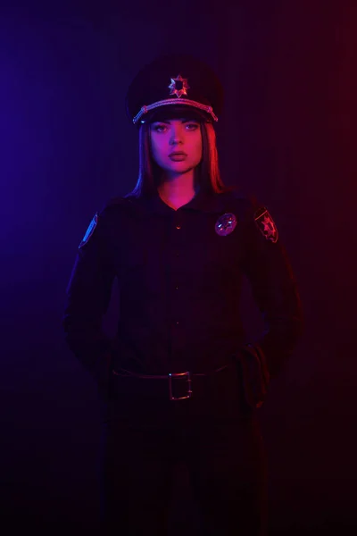 Kızıl saçlı kadın polis memuru kırmızı ve mavi arka aydınlatma ile siyah bir arka plan karşı kamera için poz. — Stok fotoğraf