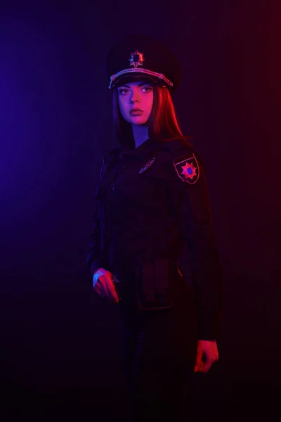 Une policière rousse pose pour la caméra sur un fond noir avec un rétroéclairage rouge et bleu . — Photo