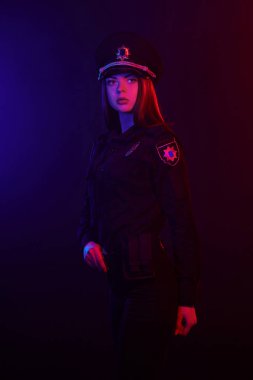 Kızıl saçlı kadın polis memuru kırmızı ve mavi arka aydınlatma ile siyah bir arka plan karşı kamera için poz.
