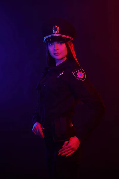 Rödhåriga kvinnlig polis är poserar för kameran mot en svart bakgrund med röd och blå bakgrundsbelysning. — Stockfoto