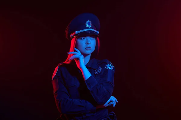 Zbliżenie strzał z redheaded kobieta policjant jest stwarzające dla kamery na czarnym tle z czerwonym i niebieskim podświetleniem. — Zdjęcie stockowe