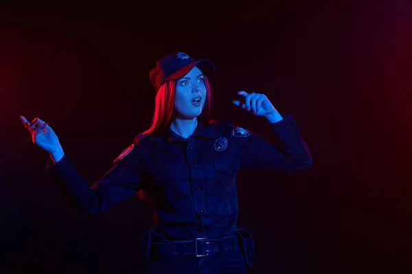 Close-up shot of a redheaded female police officer is posing for the camera against a black background with red and blue backlighting. — Stock Photo, Image