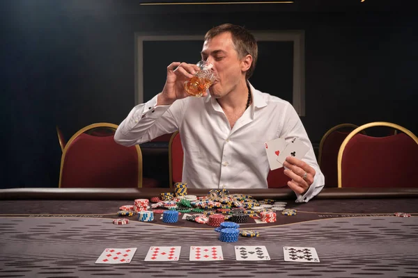 Hombre guapo emocional está jugando póquer sentado en la mesa en el casino . — Foto de Stock