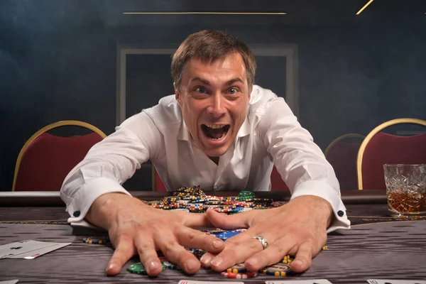 Hombre guapo emocional está jugando póquer sentado en la mesa en el casino . — Foto de Stock