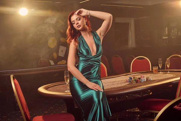 Młoda piękna kobieta pozuje przeciwko stołowi pokerowemu w luksusowym kasynie. — Zdjęcie stockowe