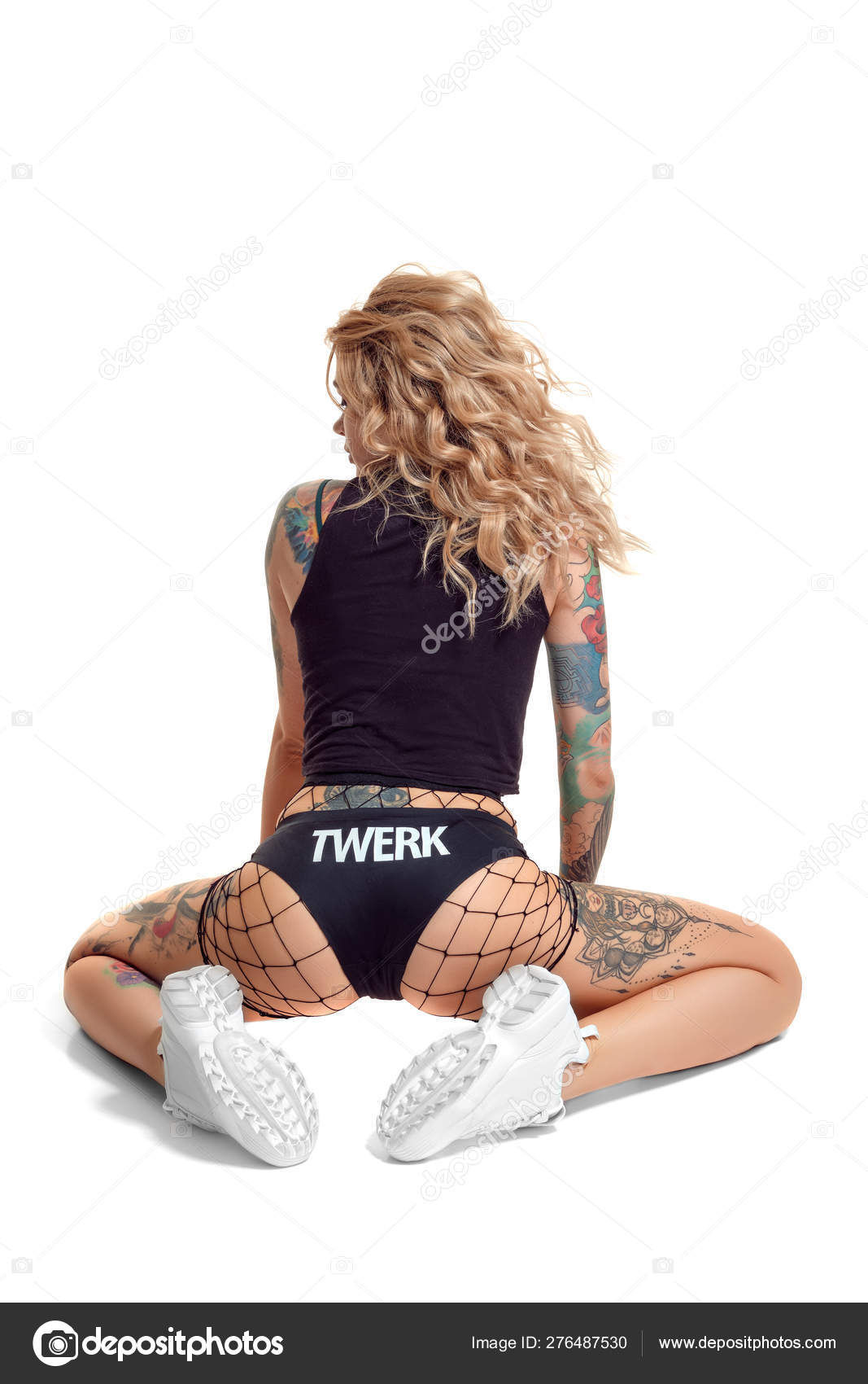 Sexy blond twerk woman with tattoed body and long curly hair is posing in s...