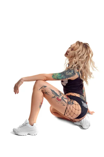 Sexy blonde twerk femme avec le corps tatoué et les cheveux longs bouclés pose en studio . — Photo