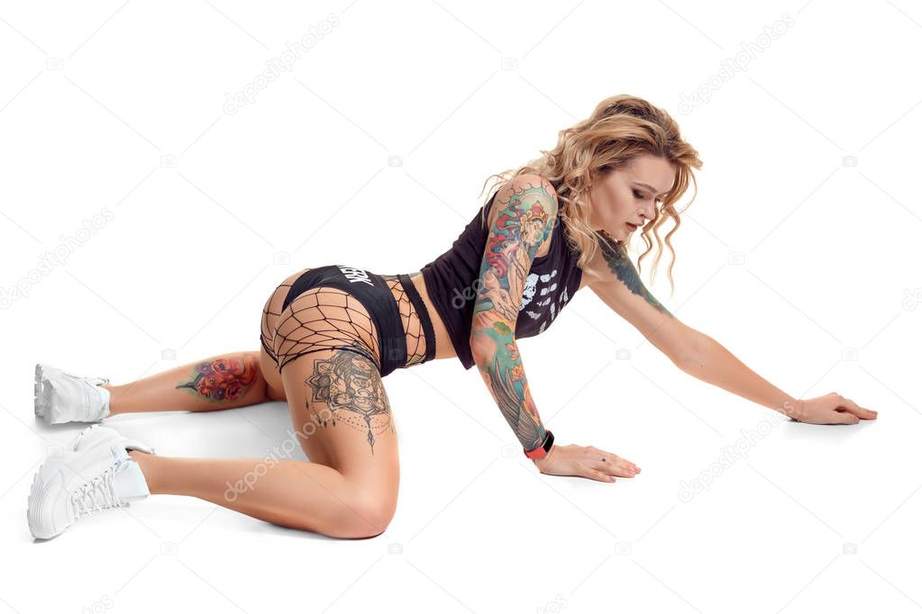 Sexy blond twerk woman with tattoed body and long curly hair is posing in studio.