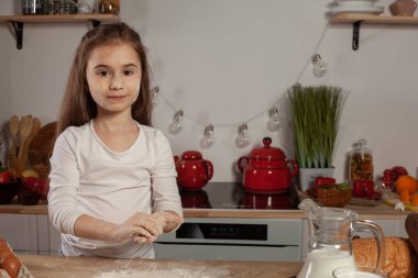 Beyaz bir bluz giymiş güzel küçük kız bir mutfakta bir ekmek pişirme için bir hamur yapıyor.