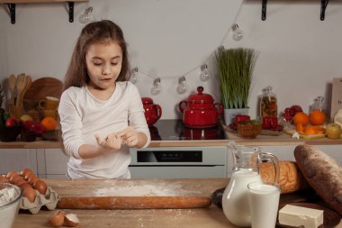 Beyaz bir bluz giymiş güzel küçük kız bir mutfakta bir ekmek pişirme için bir hamur yapıyor.