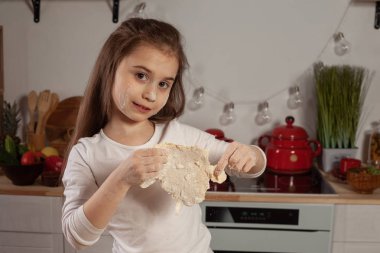 Beyaz bir bluz giymiş güzel küçük kız bir mutfakta bir ekmek pişirme için bir hamur yapıyor.