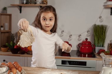 Beyaz bir bluz giymiş güzel küçük kız bir mutfakta bir ekmek pişirme için bir hamur yapıyor.