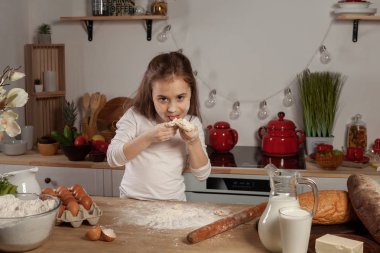 Beyaz bir bluz giymiş güzel küçük kız bir mutfakta bir ekmek pişirme için bir hamur yapıyor.