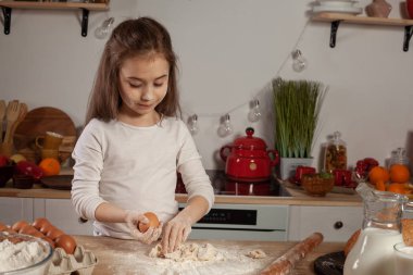 Beyaz bir bluz giymiş güzel küçük kız bir mutfakta bir ekmek pişirme için bir hamur yapıyor.
