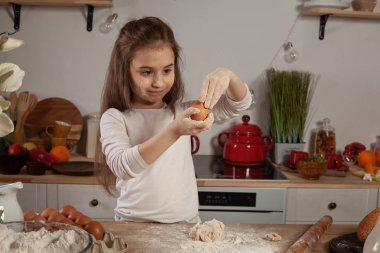 Beyaz bir bluz giymiş güzel küçük kız bir mutfakta bir ekmek pişirme için bir hamur yapıyor.