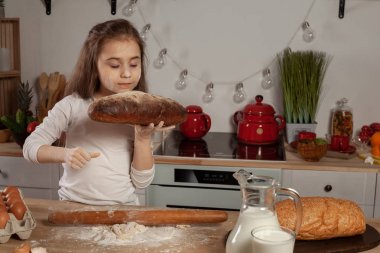Beyaz bir bluz giymiş güzel küçük kız bir mutfakta bir ekmek pişirme için bir hamur yapıyor.