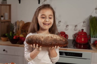 Beyaz bir bluz giymiş güzel küçük kız bir mutfakta bir ekmek pişirme için bir hamur yapıyor.