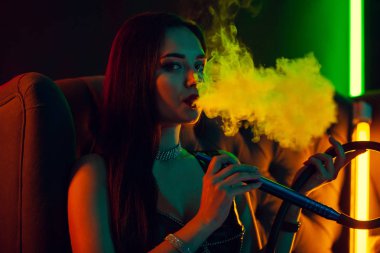 Seksi esmer model lüks bir gece kulübünde bir duman nefes bir nargile içiyor.