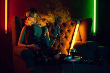 Seksi esmer model lüks bir gece kulübünde bir duman nefes bir nargile içiyor.